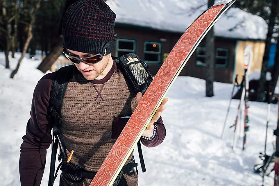 Man in beanie and sunglasses carrying skis